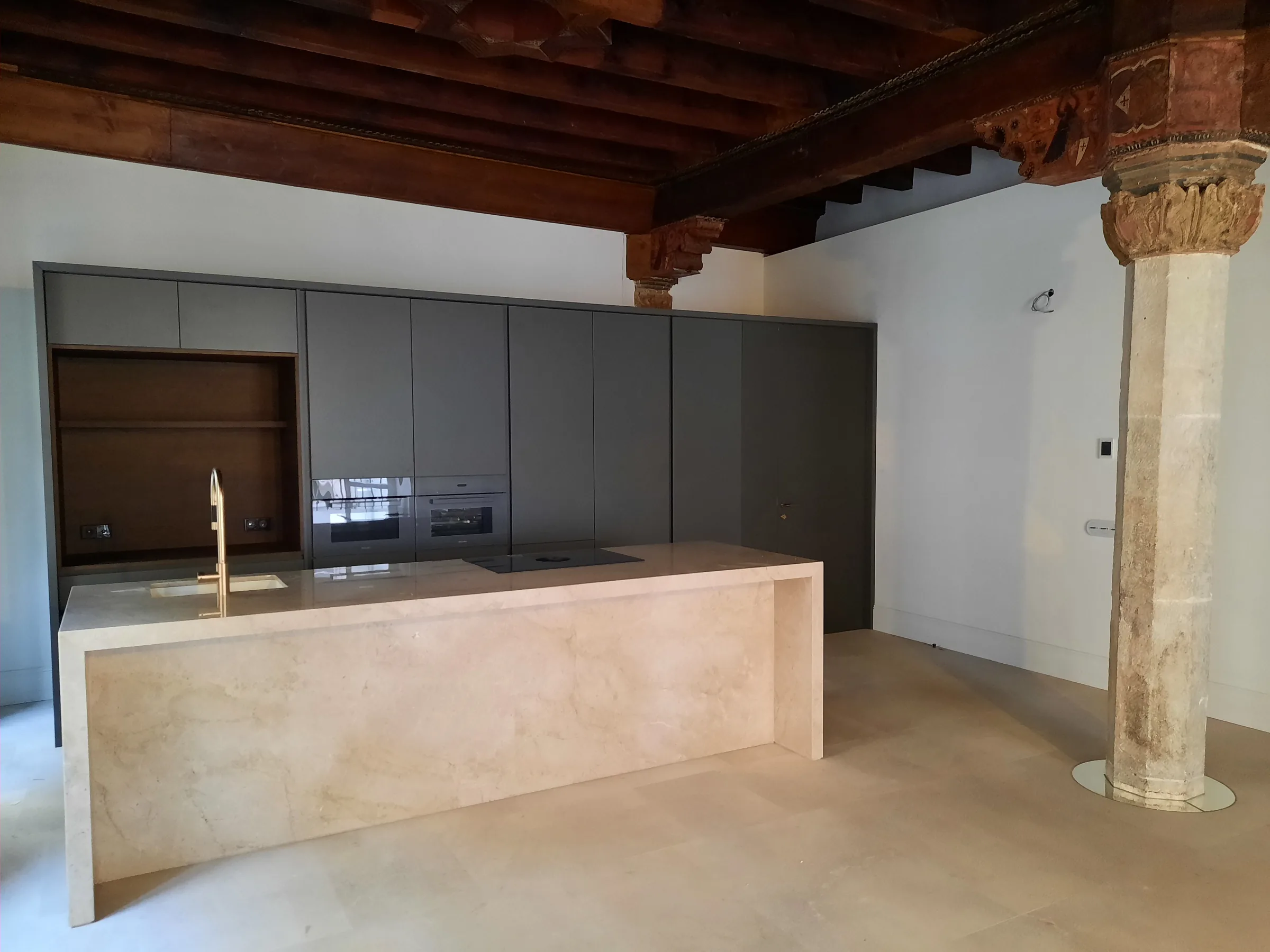 Cocina de un edificio histórico rehabilitado en el centro de Palma, con columna original de piedra y vigas de madera.